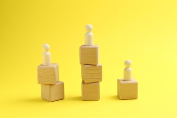 Human figures on stacked wooden cubes against yellow background. Competition concept
