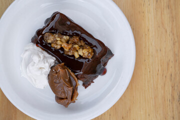 Sweet desserts. Top view of a bittersweet chocolate flan with vanilla cream and dulce de leche, in a white dish on the wooden table