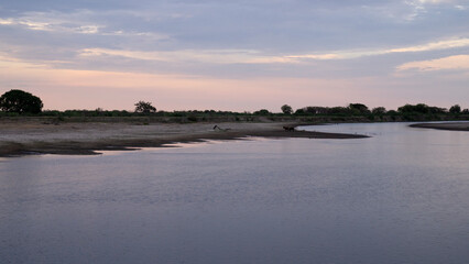 Magical view of the river and shore under a sunset sky with beautiful clouds. Enchanting reflection of the dusk colors in the water surface