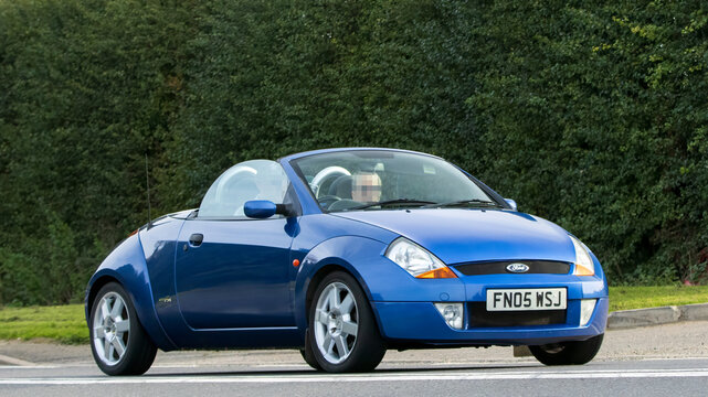 2005 blue convertible Ford Ka classic car driving on an English country road.