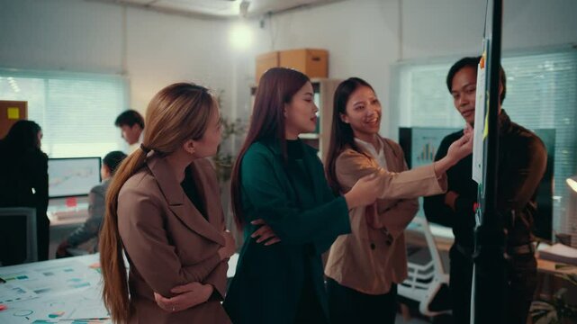 Young asian businesswoman leading a presentation to colleagues, explaining charts and graphs on a whiteboard, fostering collaboration and strategic decision-making in a modern office environment