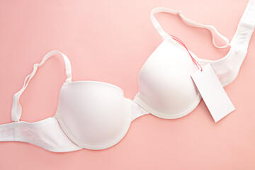 White women's bra with white paper label on pink background