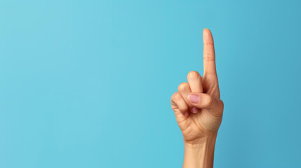 A female hand elegantly displaying the number one, with an index finger pointed upwards against a light blue backdrop.