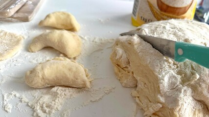 Traditional Ukrainian dish, Preparing Dough and Crafting Dumplings on a Flour-Dusted Surface. Homemade dumpling preparation in progress, featuring dough, a knife, and ingredients on a white surface.
