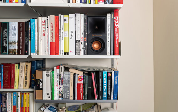 Paris, France - Apr 18, 2023: A cleanly arranged bookshelf featuring an elegant speaker Klipsch Reference with a golden cone surrounded by colorful design and art book on vitsoe shelves