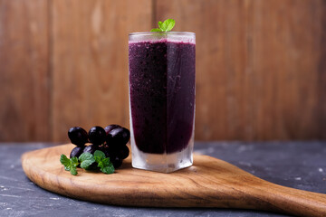 a glass of black grape juice on a wooden background.