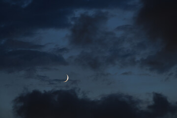 The thin sliver of a crescent moon glows softly against a late evening sky filled with dark, ominous wispy clouds. The mystical scene is mesmerizing and evokes images of Halloween. © thomasgweber