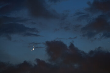 A crescent moon dances with Venus on a blue backdrop as night fall slowly blankets an evening sky dotted with wispy clouds showing hues of purple and orange. © thomasgweber