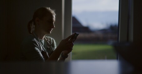 Silhouette of a woman browsing smartphone in front of a kitchen window