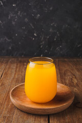 glass of orange juice on an old wooden table, with a patterned black background