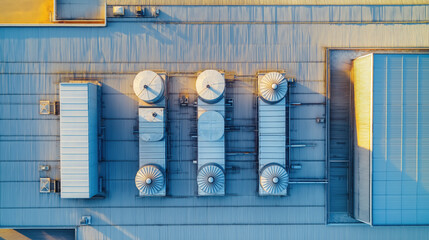 Overhead View of a Large Industrial Warehouse with Metal Roofing and HVAC Units, Set Against a Sunny, Blue Sky Backdrop