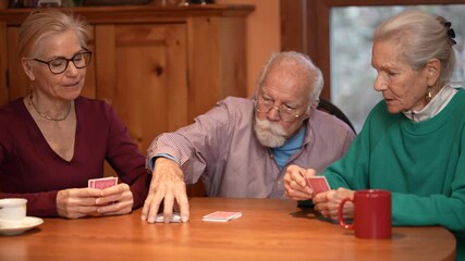 Family members gather around a wooden table playing cards and sharing laughter in a cozy living room. The elderly couple relishes quality time with their daughter. - Powered by Adobe