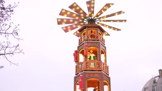 A beautifully illuminated wooden Christmas pyramid tower decorates the Paris Christmas market, adding warmth and tradition to the festive scene. 