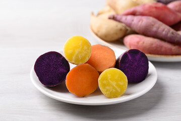 Steamed purple, orange and yellow sweet potatoes on plate ready to eating on white background