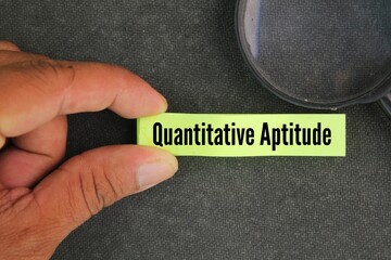 magnifying glass and paper with the word quantitative aptitude. tests a candidate's mathematical skills and analytical ability which is put to use in every step of life and career