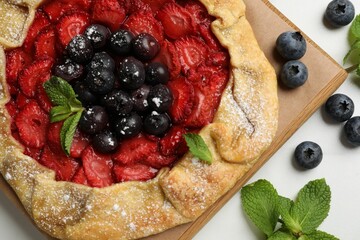 Tasty galette with berries and mint on white table, flat lay