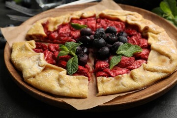 Tasty galette with strawberries, blueberries and mint on dark gray textured table, closeup
