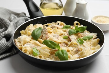 Delicious pasta Alfredo with chicken, cheese and basil in frying pan on white table, closeup