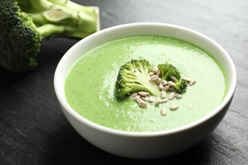 Delicious broccoli cream soup in bowl on black table, closeup