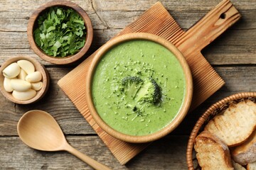 Delicious broccoli cream soup served on wooden table, flat lay