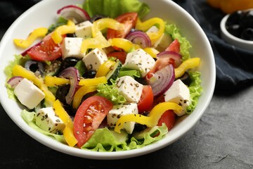 Delicious fresh Greek salad in bowl on black table, closeup