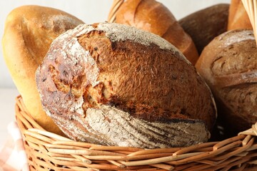 Different freshly baked bread loafs in wicker basket on table, closeup