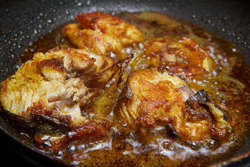 close-up of seasoned or marinated fish pieces frying in coconut oil, golden brown crispy fish with bubbling and glistening oil, side angle view with selective focus and copy space