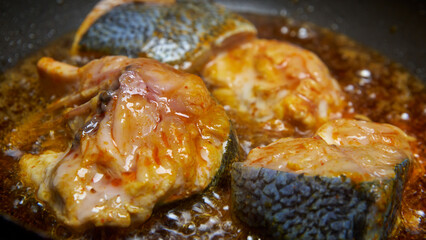 close-up of seasoned or marinated fish pieces frying in coconut oil, golden brown crispy fish with bubbling and glistening oil, side angle view with selective focus and copy space