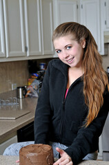 Beautiful young Caucasian woman relaxing in kitchen smiling in front of chocolate cake.