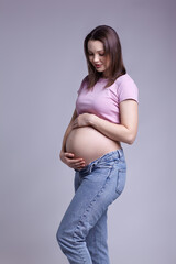 Young pretty pregnant woman in pink t-shirt and jeans on gray background.