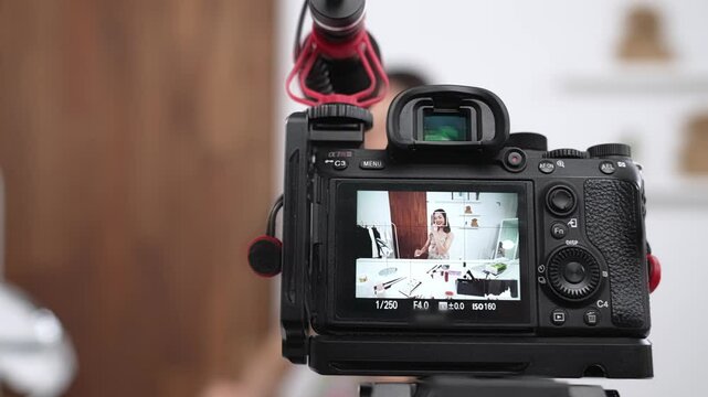 Rear view behide camera screen display woman influencer shoot live streaming vlog video review skincare social media or blog. Girl with cosmetic vivancy studio lighting for marketing recording.