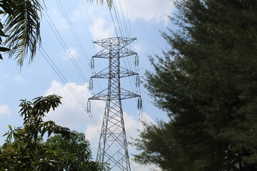High voltage electrical towers and lines, among the trees, cloudy blue sky background