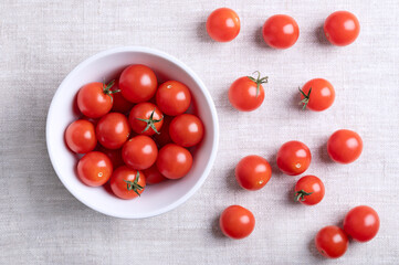 Small red cherry tomatoes in a white bowl on linen fabric, from above. Fresh, ripe, tiny and round cocktail tomatoes of the type Solanum lycopersicum var. cerasiforme, of juicy and sweet taste.