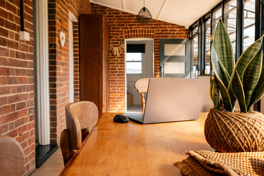 Cosy home office with laptop on wooden table, brick walls, and natural light.