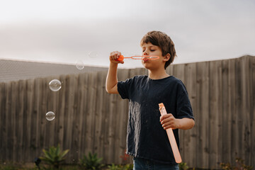 Young boy in black shirt blowing bubbles in their yard.