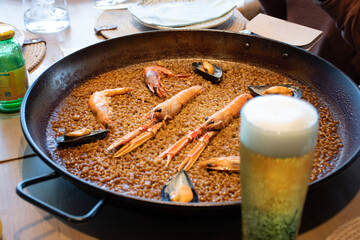 Spanish Valencian paella with traditional rice and seafood with crayfish and shrimps . seafood pairing with blurred beer in a restaurant
