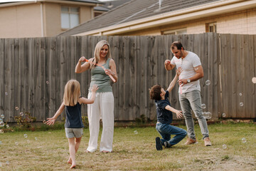 Happy family blowing and playing with bubbles in their yard.