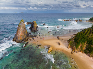 Aerial view of jagged rock formations off a sandy beach and rugged coastline