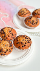 Delicious chocolate chip muffins on white plates in soft pink setting. Birthday concept