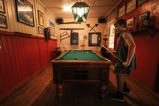 Teenage male playing 8 ball pool on billiard table in Australian pub