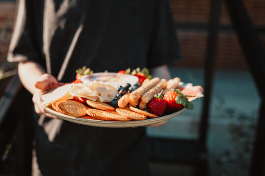 Hand holding platter with crackers, breadsticks, strawberries, and berries.