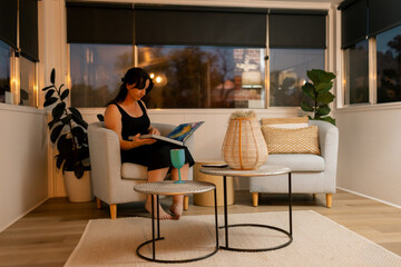 Woman reading on sofa in cosy modern living room with plants and stylish evening decor