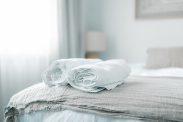 Freshly folded white towels on a bed in a serene, softly lit bedroom for relaxation