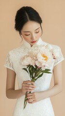 Elegant woman in traditional white dress holding peony bouquet against soft neutral background