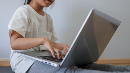 Fototapeta premium portrait of happy small pupil learning at home. Smiling little child girl enjoying doing lessons in living room. Smart kid schoolgirl looking at camera, studying remotely online. 