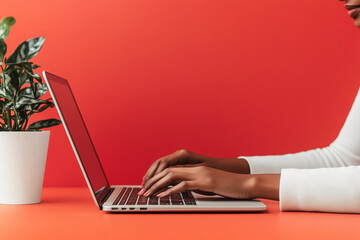 Fototapeta premium Black Woman Working on Laptop in Cozy Ember Wall Room with Houseplant - Ideal for Text and Design Backdrops