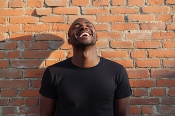 Obraz premium Handsome african american man in black t shirt laughing against brick wall