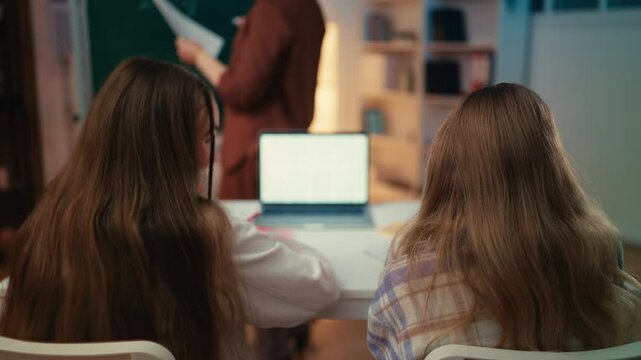 Two schoolgirls talk and laugh during a lesson at school, bad behavior in class