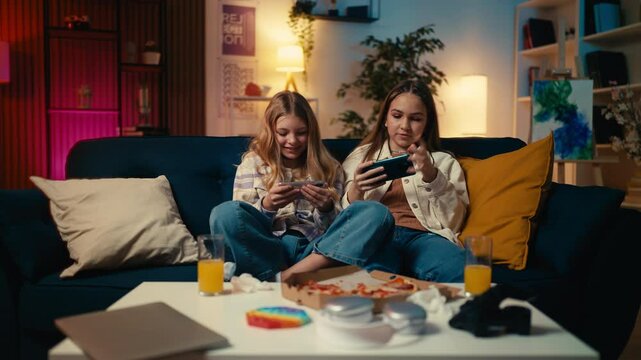 Teenage girls play an online video game on their cellphones, relaxing at home