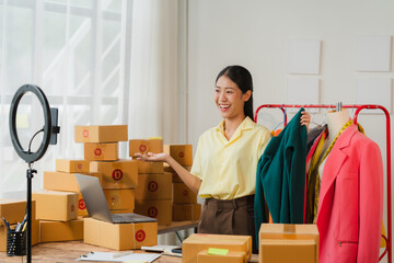 Online Fashion Entrepreneur: A young Asian woman in a bright yellow shirt stands confidently in her...
